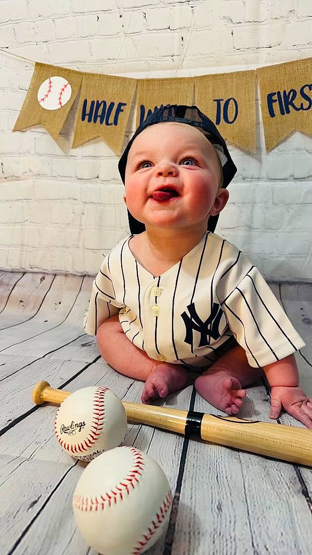 Hudson is registered to the contest to win money with this photo: baby, baby_toddler_clothing, ball, baseball, baseball_equipment, baseball_glove, bat_and_ball_games, child, face, fun, happy, membranophone, person, skin, sleeve, smile, sports_equipment, t_shirt, toddler, white