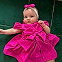 baby, child, pink_dress, headband, bow, cushion, green_cushion, infant, portrait, cute, lying_down, indoor, soft_fabric, small_hand, baby_face, baby_clothing, relaxed, looking_at_camera, child_fashion, adorable