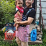 Theodore is registered to the contest to win money with this photo: adult, baby, child, person, smile, outdoor, garden, plants, grass, watering_can, steps, crate, plates, doorway, overalls, clothing, greenery, yard, summer, holding