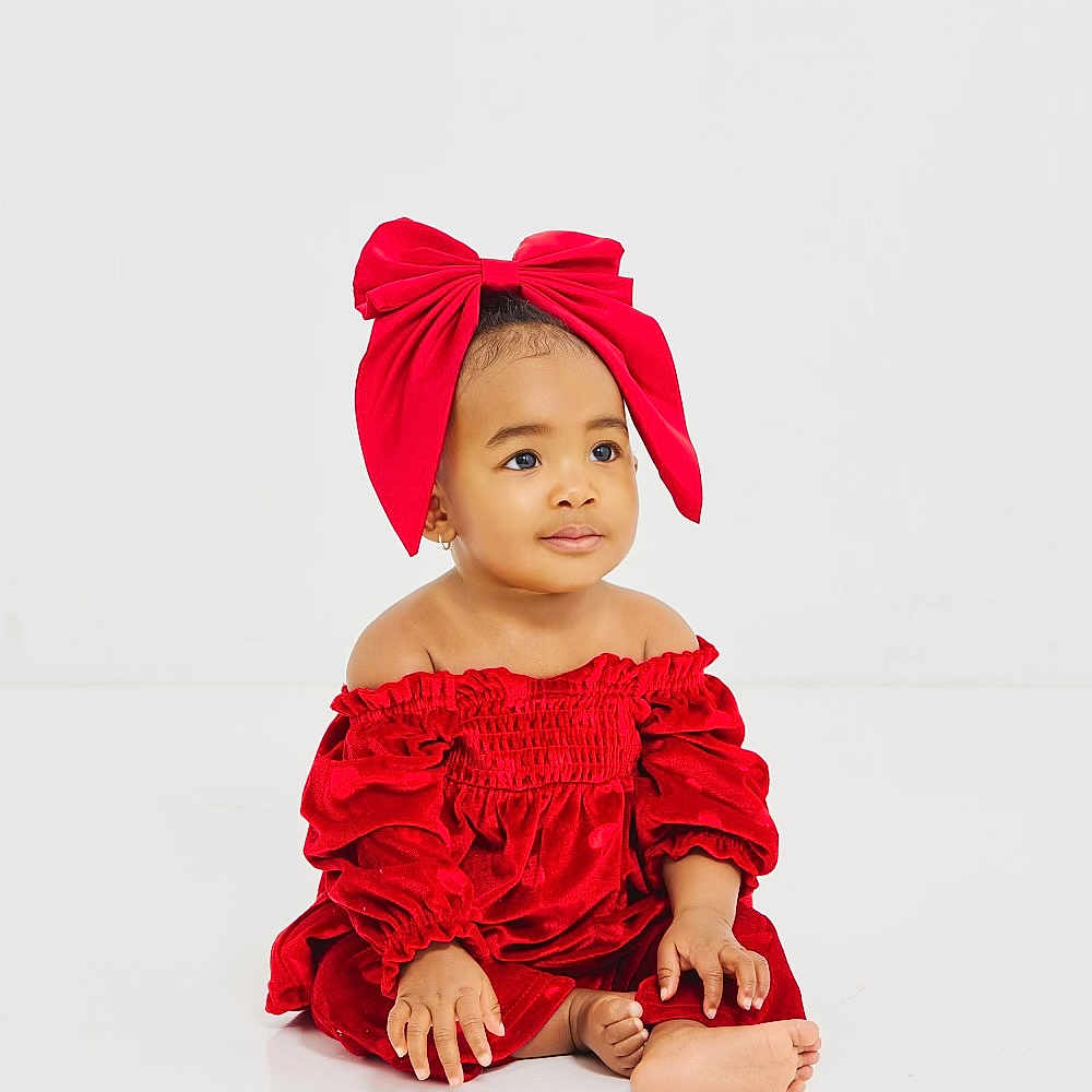 Azaiya Green is registered to the contest to win money with this photo: adorable, baby, barefoot, calm, child, cute, fashion, feet, hands, headwear, indoor, infant, portrait, red_bow, red_dress, sitting, smiling, studio_photo, white_background, young_child