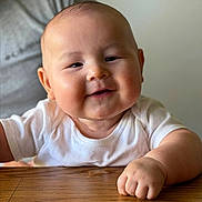 Sam joined the competition — help win amazing prizes! arm, baby, child, chubby, closeup, cute, drool, expression, face, hand, happy, indoor, infant, person, portrait, skin, smiling, white_shirt, wooden_table, young