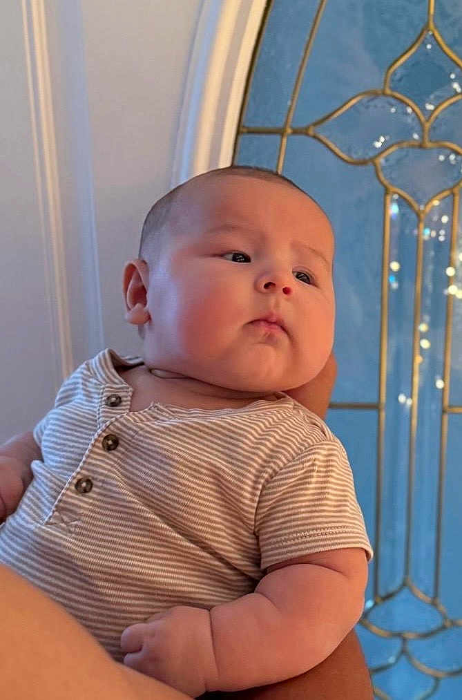 Sam joined the competition — help win amazing prizes! baby, child, infant, striped_shirt, arm, face, person, indoor, window, glass, decorative_window, blue, gold, skin, portrait, expression, holding, cute, young, chubby