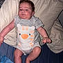 baby, infant, child, onesie, clothing, bed, pillow, blanket, blue_bedding, cream_pillow, person, face, skin, hand, foot, lying_down, indoors, sleepwear, cute, expression