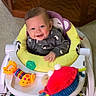 baby, child, smiling, sitting, activity_walker, infant, portrait, indoor, toy, pacifier, colorful, playtime, furniture, carpet, wooden_background, gray_clothing, stuffed_animal, baby_gear, happy, face