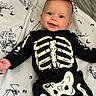 baby, child, infant, smiling, portrait, skeleton_costume, halloween, black_clothing, white_bones, bedding, blanket, bed, lying_down, indoors, face, blue_eyes, happy, cartoon_print, spooky, photography