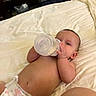 baby, infant, bottle, feeding, bed, blanket, bedroom, diaper, lying_down, face, hands, portrait, indoors, home, furniture, sleeping_area, milk, bald, relaxed, parent