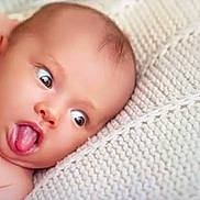 Lily is registered to the contest to win money with this photo: baby, child, closeup, cute, expression, face, funny_face, head, indoors, infant, knitted_blanket, lying_down, newborn, person, portrait, skin, soft, texture, tongue, wide_eyes