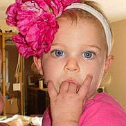 Helena is registered to the contest to win money with this photo: toddler, child, headband, flower, pink_clothing, indoor, portrait, blue_eyes, cute, baby, person, young_child, hand, face, hair, room, home, looking_at_camera, expression, casual