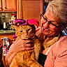 Phatkat is registered to the contest to win money with this photo: cat, cats, orange_cat, jester_hat, costume, pet, person, woman, glasses, smiling, kitchen, indoor, portrait, pet_photography, holding, furry, whiskers, wooden_cabinets, background_cat, humorous