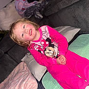 Oakley is registered to the contest to win money with this photo: child, smiling, pajamas, pink, minnie_mouse, face, indoor, blanket, couch, pillow, happy, seated, person, clothing, cute, cozy, home, young, portrait, fun