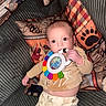 Carson joined the competition — help win amazing prizes! baby, infant, toy, colorful, pillow, couch, patterned, clothing, hand, face, wide_eyes, indoor, cozy, child, sitting, blanket, cute, playful, fabric, home