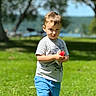 child, boy, grass, outdoor, summer, popsicle, greenery, tree, nature, casual_clothing, shorts, tshirt, daylight, portrait, standing, sunlight, recreation, playful, happy, vacation