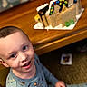 child, boy, pajamas, smiling, face, indoor, table, gingerbread_house, wood, food, messy_face, holiday, festive, happy, person, seated, closeup, background_blur, home, cute