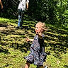 child, toddler, running, outdoor, grass, sunlight, trees, adult, casual_clothing, shadows, nature, playful, dress, sneakers, joyful, summer, park, greenery, person, daylight