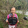 child, kindergarten, first_day, sign, outdoor, smiling, backpack, hoodie, grass, trees, nature, young_child, person, celebration, happy, portrait, casual_clothing, school, daylight, holding