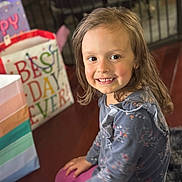 Aurora is registered to the contest to win money with this photo: child, smiling, indoor, gift_bags, colorful, floor, long_hair, blue_top, pink_leggings, sitting, happy, face, person, celebration, party, blurred_background, flooring, metal_gate, portrait, young_girl