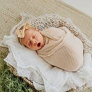 Ella joined the competition — help win amazing prizes! newborn, baby, yawning, wrapped, blanket, headband, bow, knitted_cushion, white_fabric, greenery, cozy, sleeping, infant, soft_texture, resting, cute, peaceful, portrait, indoors, warm_colors