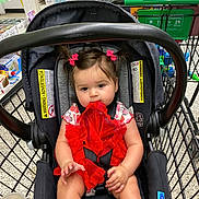 Vayda is registered to the contest to win money with this photo: baby, child, car_seat, shopping_cart, red_dress, hair_bows, girl, fabric, store, retail, product_shelves, floor, plastic_cup, seat_belt, person, indoor, shopping, cute, infant, chewing