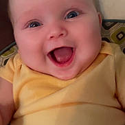 Gracelyn is registered to the contest to win money with this photo: baby, smiling, happy, infant, yellow_clothing, face, blue_eyes, cushion, patterned_background, child, cute, portrait, indoors, young, cheerful, skin, head, person, expression, sitting