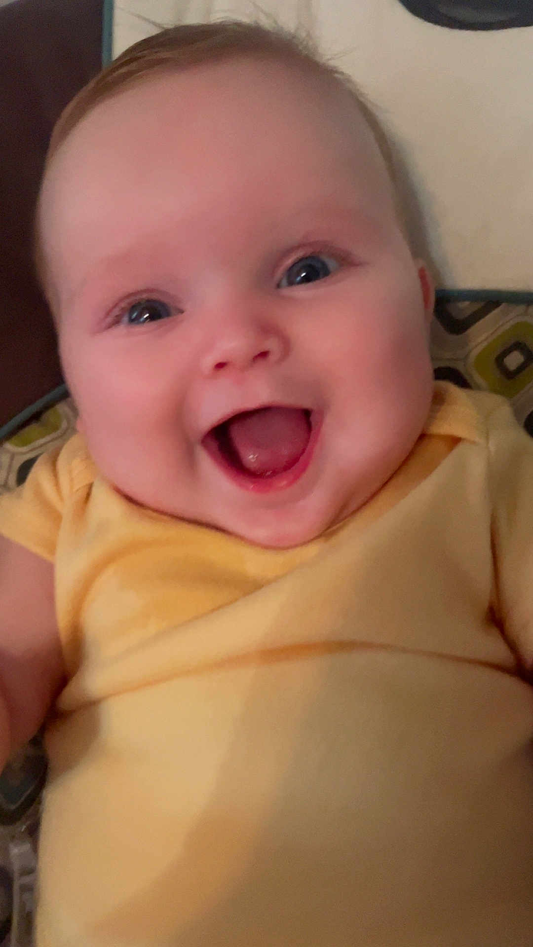 Gracelyn is registered to the contest to win money with this photo: baby, smiling, happy, infant, yellow_clothing, face, blue_eyes, cushion, patterned_background, child, cute, portrait, indoors, young, cheerful, skin, head, person, expression, sitting