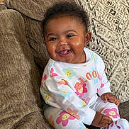 Kyomi is registered to the contest to win money with this photo: baby, child, smiling, sitting, couch, clothing, floral_pattern, happy, indoors, person, cute, face, sock, pajamas, home, infant, young_child, cozy, portrait, bright