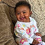 baby, child, smiling, sitting, couch, clothing, floral_pattern, happy, indoors, person, cute, face, sock, pajamas, home, infant, young_child, cozy, portrait, bright