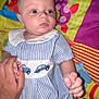 Reggie is registered to the contest to win money with this photo: baby, infant, hand, striped_clothing, blue, white, playmat, colorful, pattern, car_print, person, child, indoor, holding_hand, cute, young, face, eyes, skin, portrait