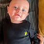 baby, infant, face, blue_eyes, black_clothing, yellow_logo, hand, blanket, striped_fabric, lying_down, cute, portrait, child, skin, head, smile, human, young, tender, cozy