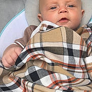 Reggie is registered to the contest to win money with this photo: baby, blanket, plaid, infant, child, face, blue_eyes, clothing, seat, comfort, indoor, portrait, cute, young, skin, expression, hand, head, soft, resting