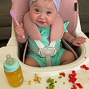 Kayliese joined the competition — help win amazing prizes! baby, high_chair, spoon, baby_bottle, fruit, kiwi, watermelon, banana, headband, bow, green_clothing, pink_spoon, feeding_time, smiling, child, indoor, couch, seat_belt, cute, happy