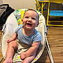 baby, smiling, baby_rocker, blue_shirt, indoor, wooden_floor, child, furniture, yellow_chair, yellow_table, happy, cute, infant, seat, toys, playroom, person, legs, feet, face