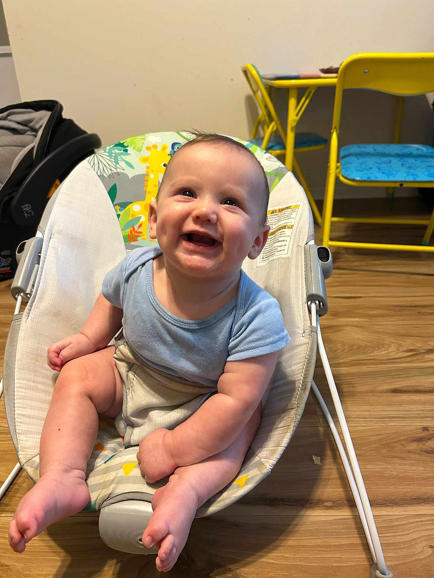 Raiden joined the competition — help win amazing prizes! baby, smiling, baby_rocker, blue_shirt, indoor, wooden_floor, child, furniture, yellow_chair, yellow_table, happy, cute, infant, seat, toys, playroom, person, legs, feet, face