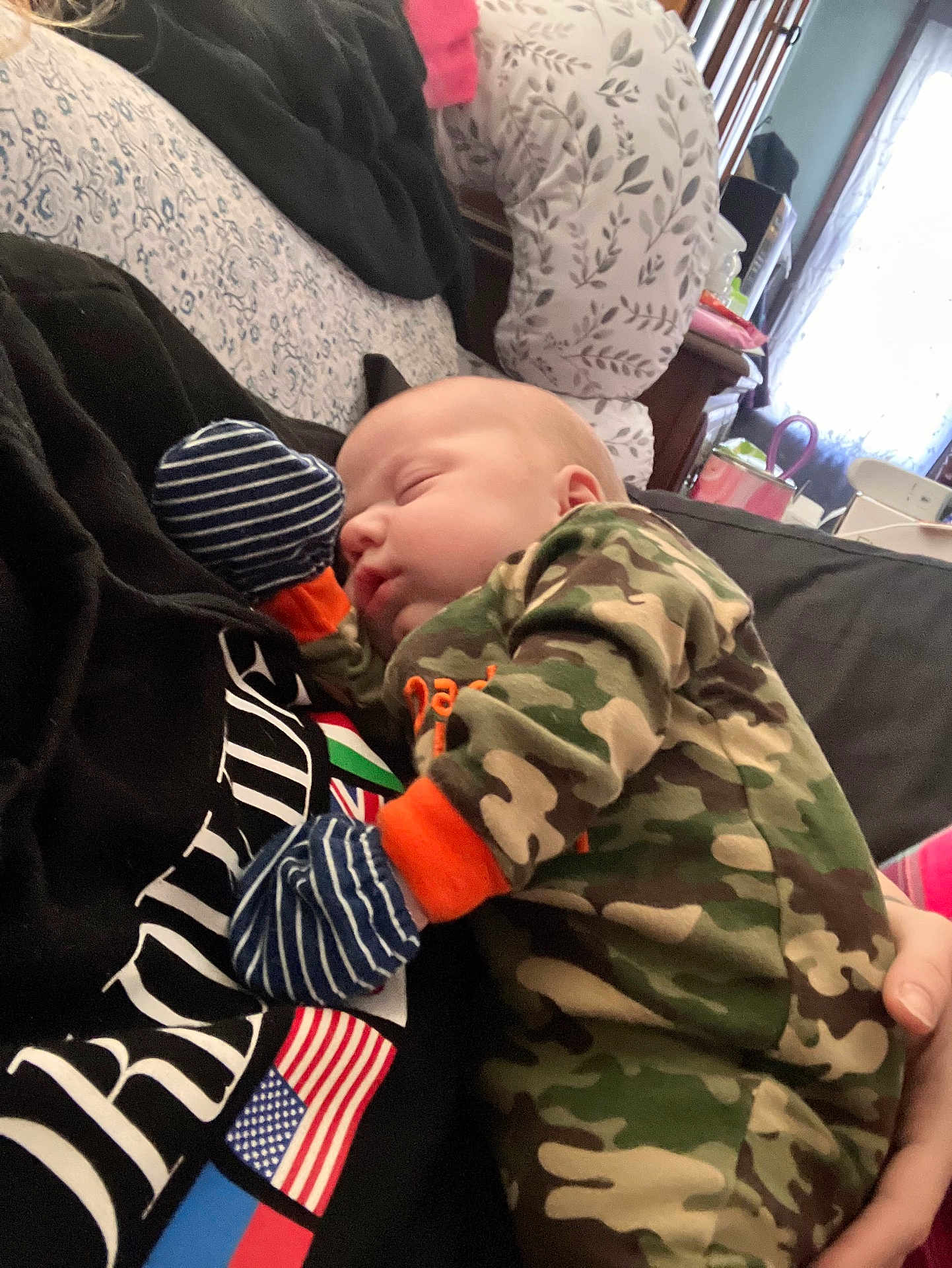 Jahseh is registered to the contest to win money with this photo: baby, infant, sleeping, camouflage, mittens, bed, pillow, blanket, toddler_clothing, person, holding, cozy, portrait, indoor, nursery_items, hand, cheek, nap, newborn, soft_fabric