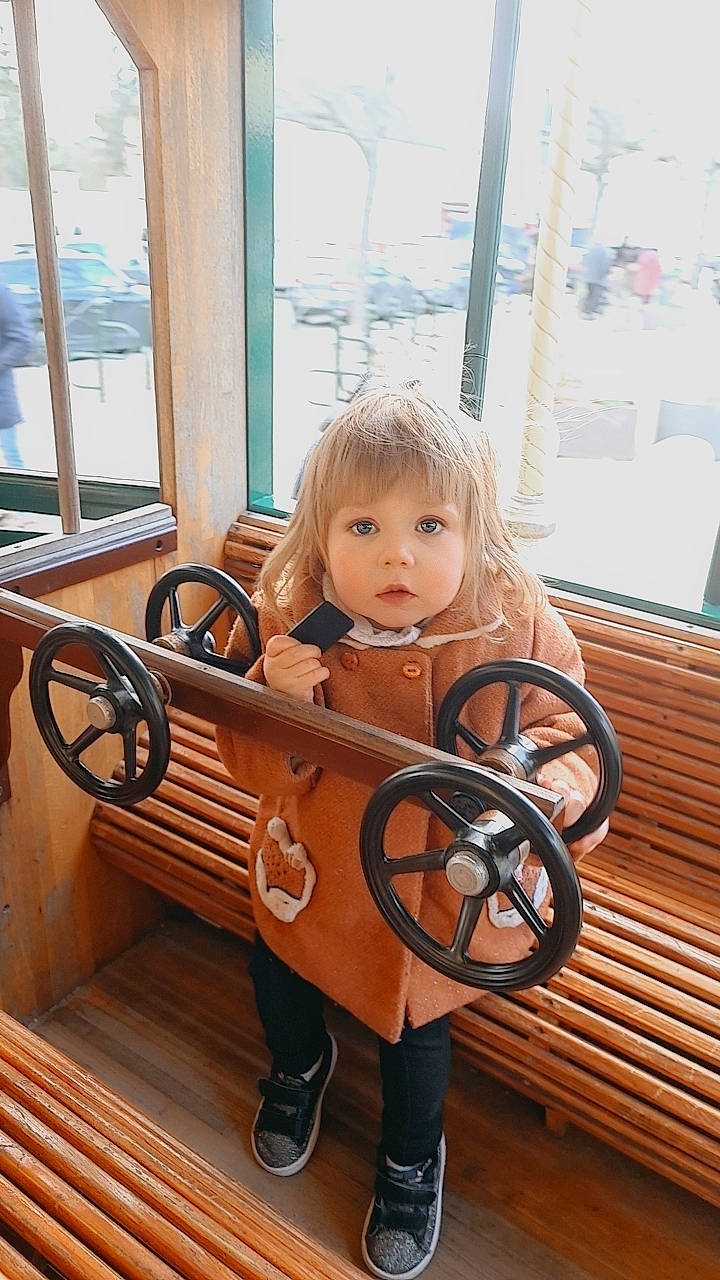 Julia a rejoint le concours — aidez-le/la à gagner de superbes lots ! auto_part, automotive_exterior, automotive_wheel_system, baby_toddler_clothing, bench, blond, dress, fun, leisure, light, metal, motor_vehicle, person, sitting, steering_wheel, tire, toddler, toy, wheel, window