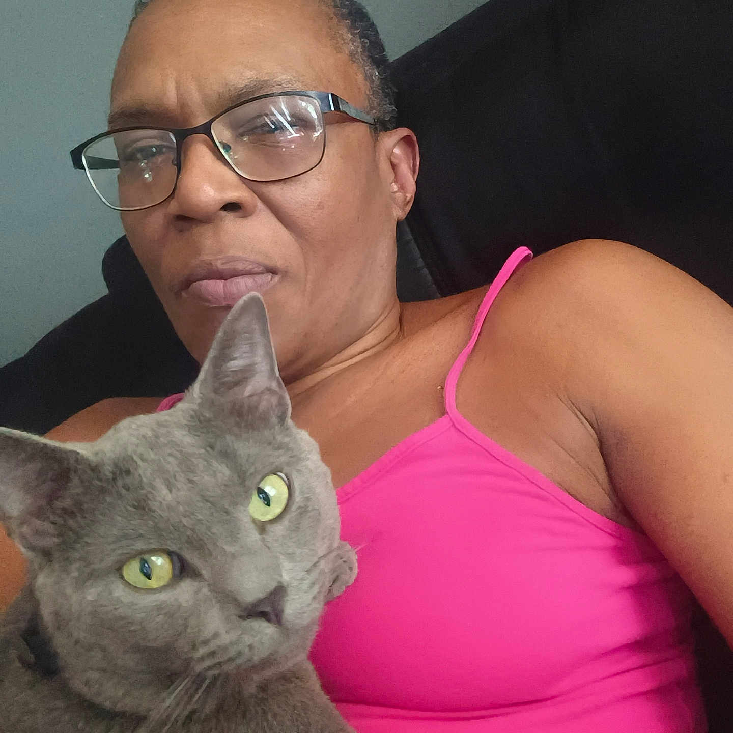 Boogie Man is registered to the contest to win money with this photo: black_background, cat, closeup, domestic_animal, ear, face, feline, glasses, gray_cat, home, indoor, person, pet, pink_clothing, portrait, relaxed, seated, shoulder, tank_top, yellow_eyes