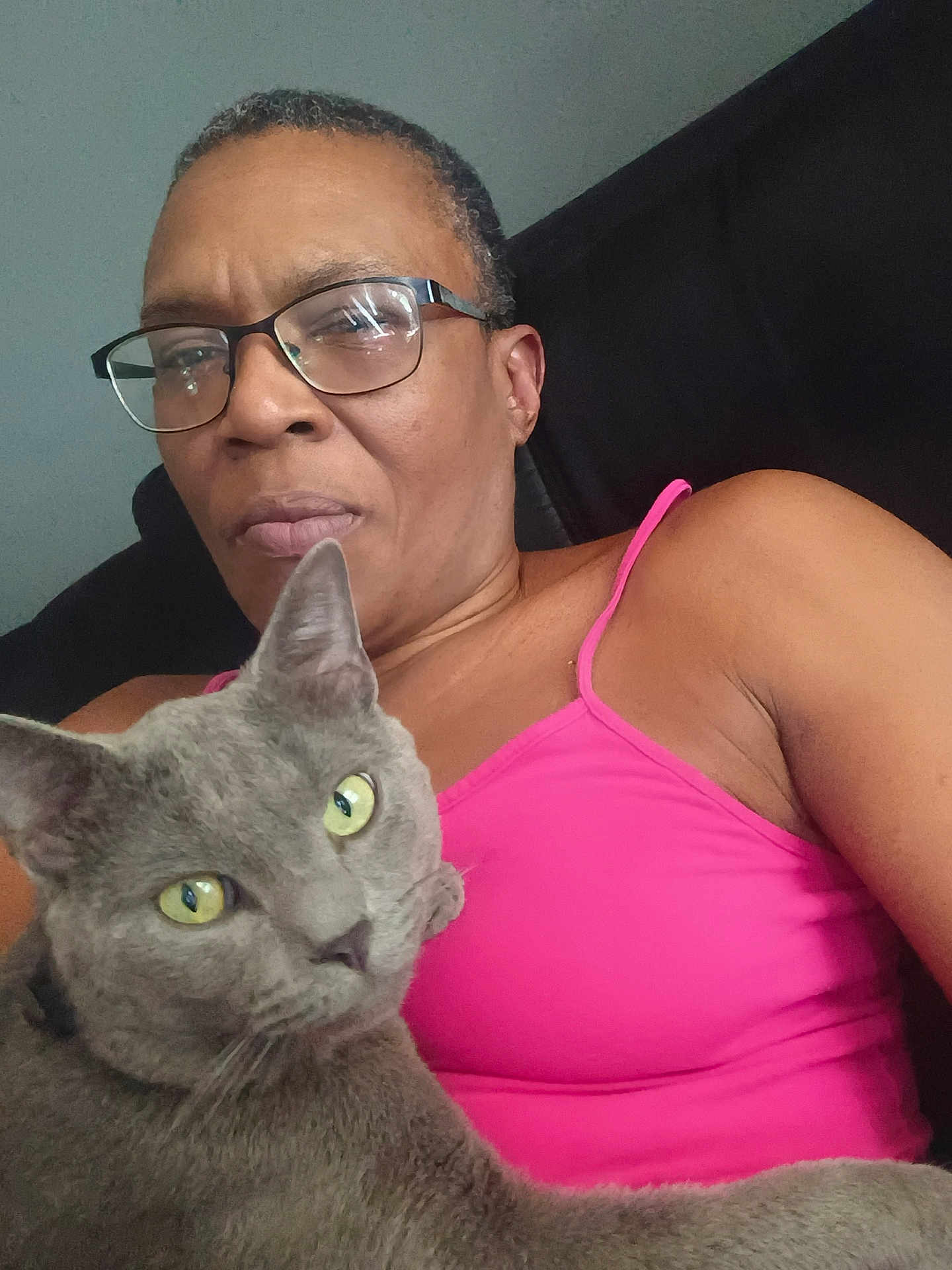 Boogie Man is registered to the contest to win money with this photo: black_background, cat, closeup, domestic_animal, ear, face, feline, glasses, gray_cat, home, indoor, person, pet, pink_clothing, portrait, relaxed, seated, shoulder, tank_top, yellow_eyes