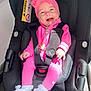 baby, car_seat, pink_clothing, headband, smiling, child, infant, safety_harness, happy, cute, indoor, footwear, white_shoes, seat, person, portrait, infant_clothing, accessory, child_safety, bright