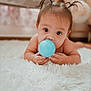 baby, child, pigtails, blue_ball, carpet, indoor, curious, cute, hands, face, eyes, infant, floor, soft, toy, young_child, lying_down, skin, person, closeup