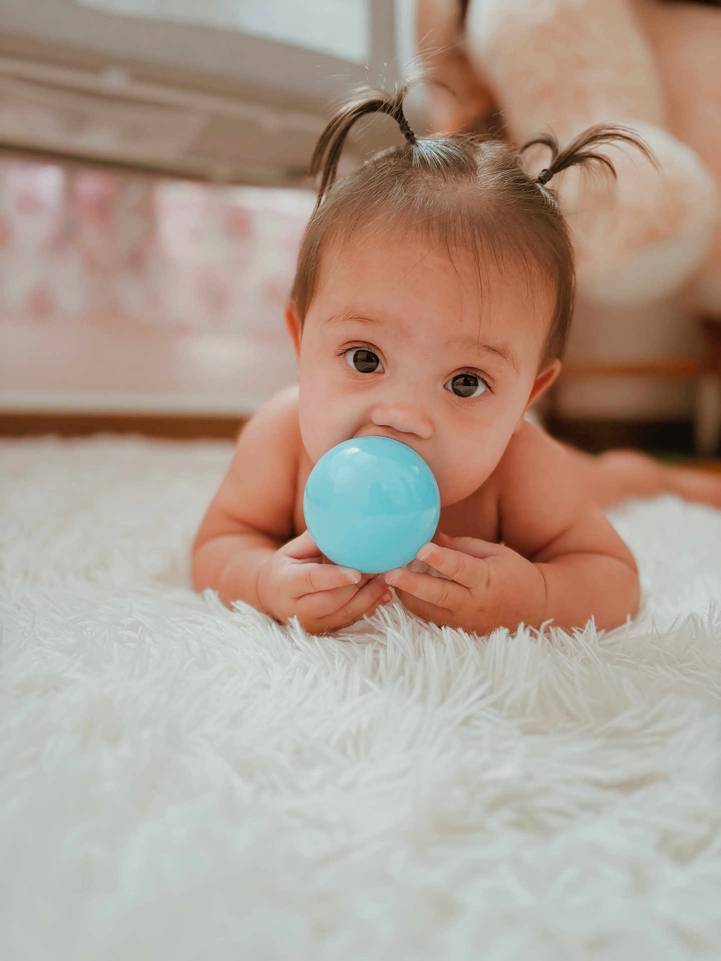 Velincia is registered to the contest to win money with this photo: baby, child, pigtails, blue_ball, carpet, indoor, curious, cute, hands, face, eyes, infant, floor, soft, toy, young_child, lying_down, skin, person, closeup
