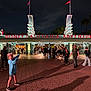 child, night, disney, california, adventure, sign, mouse_ears, hoodie, pointing, crowd, people, walking, entrance, theme_park, excited, pavement, lights, building, outdoor, fun