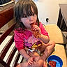 bacon, bare_feet, blue_bowl, candid, child, cookware, diaper, eating, indoor, ketchup, kitchen, long_hair, pink_hoodie, portrait, sauce, seat_cushion, snack, table, toddler, wooden_chair