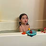 bath, bath_toy, bathroom, bathtub, child, expression, face, indoor, net, orange_ring, play, portrait, sitting, skin, surprised, toddler, toys, wall, water, wet_hair