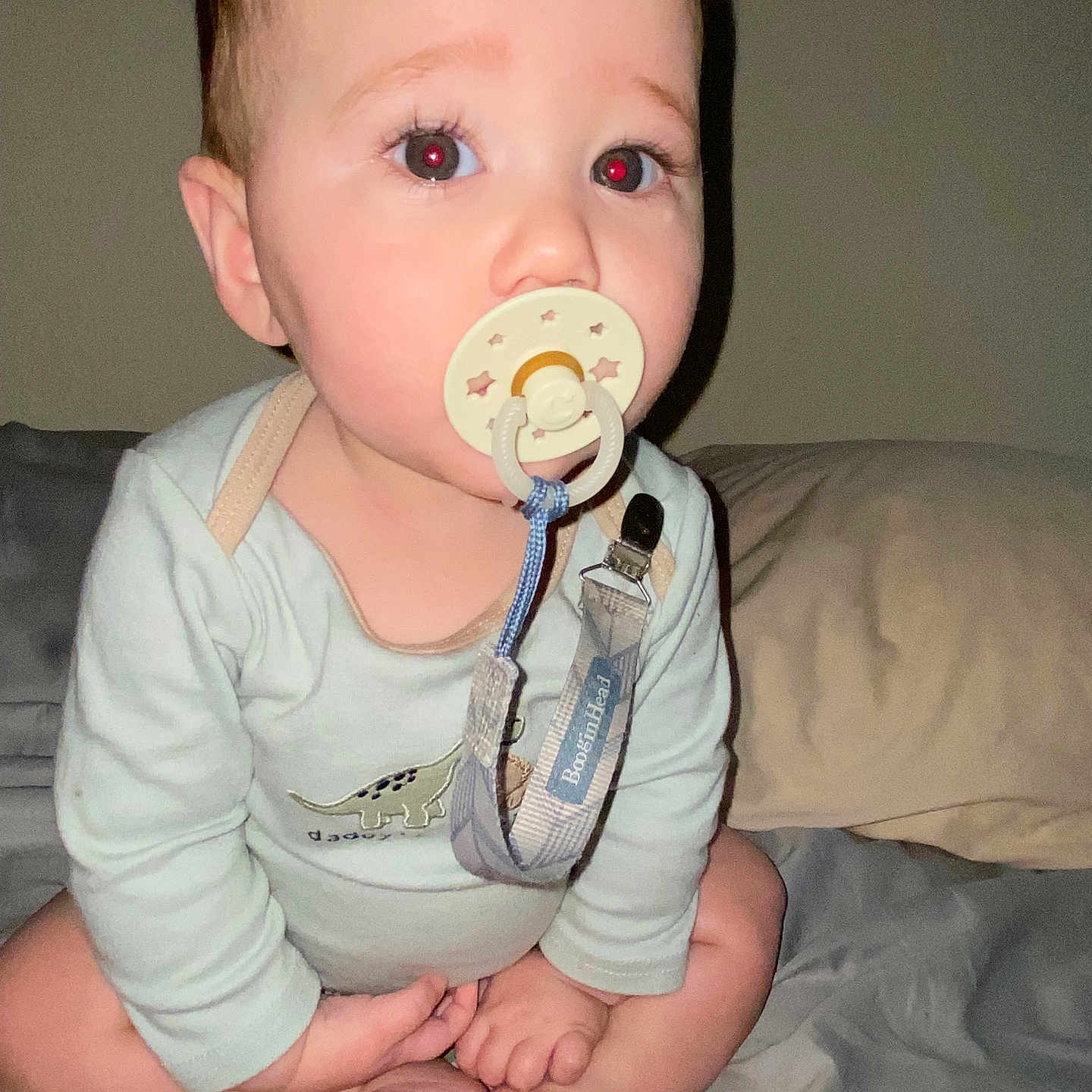 Nehemiah joined the competition — help win amazing prizes! baby, pacifier, onesie, dinosaur_print, bed, cross_legged, red_eye, infant, child, person, indoor, sleepwear, cute, face, hands, feet, skin, light, flash, expression