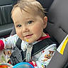 baby, child, car_seat, pajamas, toy, cup, smile, face, seatbelt, car_interior, infant, child_seat, colorful_clothing, cute, rosy_cheeks, safety_harness, indoor, closeup, happy, young_child
