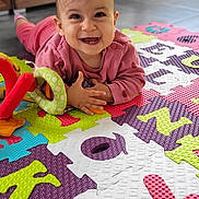 Nelly a rejoint le concours — aidez-le/la à gagner de superbes lots ! baby, child, smiling, toy, colorful_mat, indoor, floor, play, pink_clothing, happy, portrait, face, hands, head, infant, cute, home, puzzle_mat, early_learning, toddler