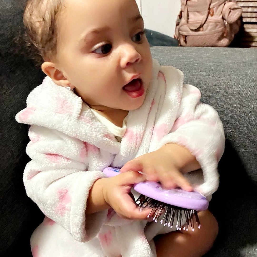 Kayla Ii is registered to the contest to win money with this photo: baby, toddler, child, hairbrush, robe, pink, white, couch, indoor, expression, face, person, seated, backpack, furniture, cute, happy, childhood, home, play