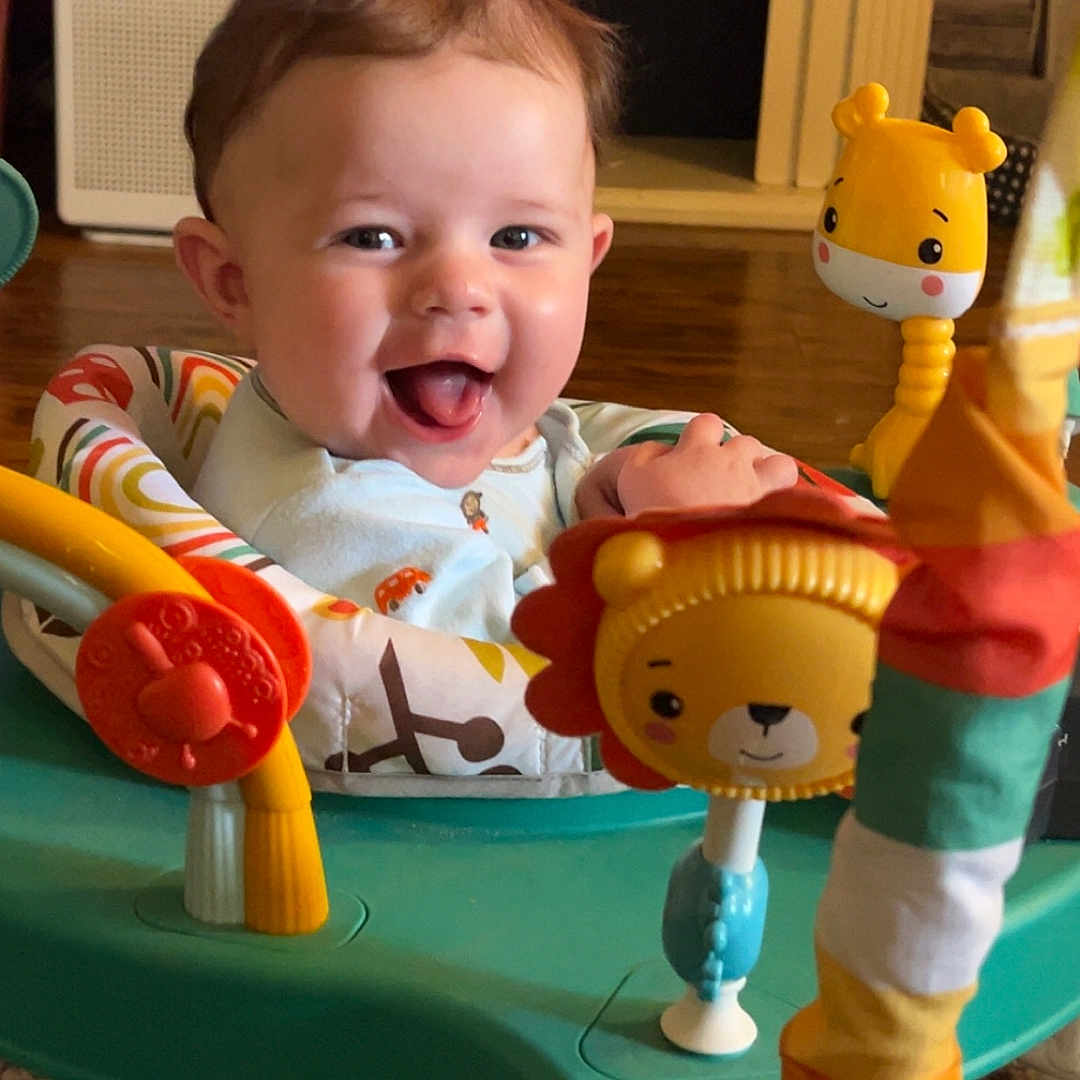 Zander is registered to the contest to win money with this photo: activity_center, baby, bright, child, clothing, colorful, cute, face, floor, furniture, happy, home, indoor, infant, joyful, person, play, seat, smiling, toys