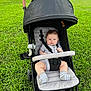 baby, stroller, grass, outdoor, child, infant, socks, onesie, seatbelt, canopy, greenery, summer, park, cute, young_child, legs, face, pavement, casual, daylight