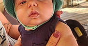 Coleson is registered to the contest to win money with this photo: baby, child, face, hat, hand, skin, nail_polish, tattoo, person, outdoor, sunlight, porch, wood, clothing, sleeveless, infant, closeup, expressionless, holding, adult_hand