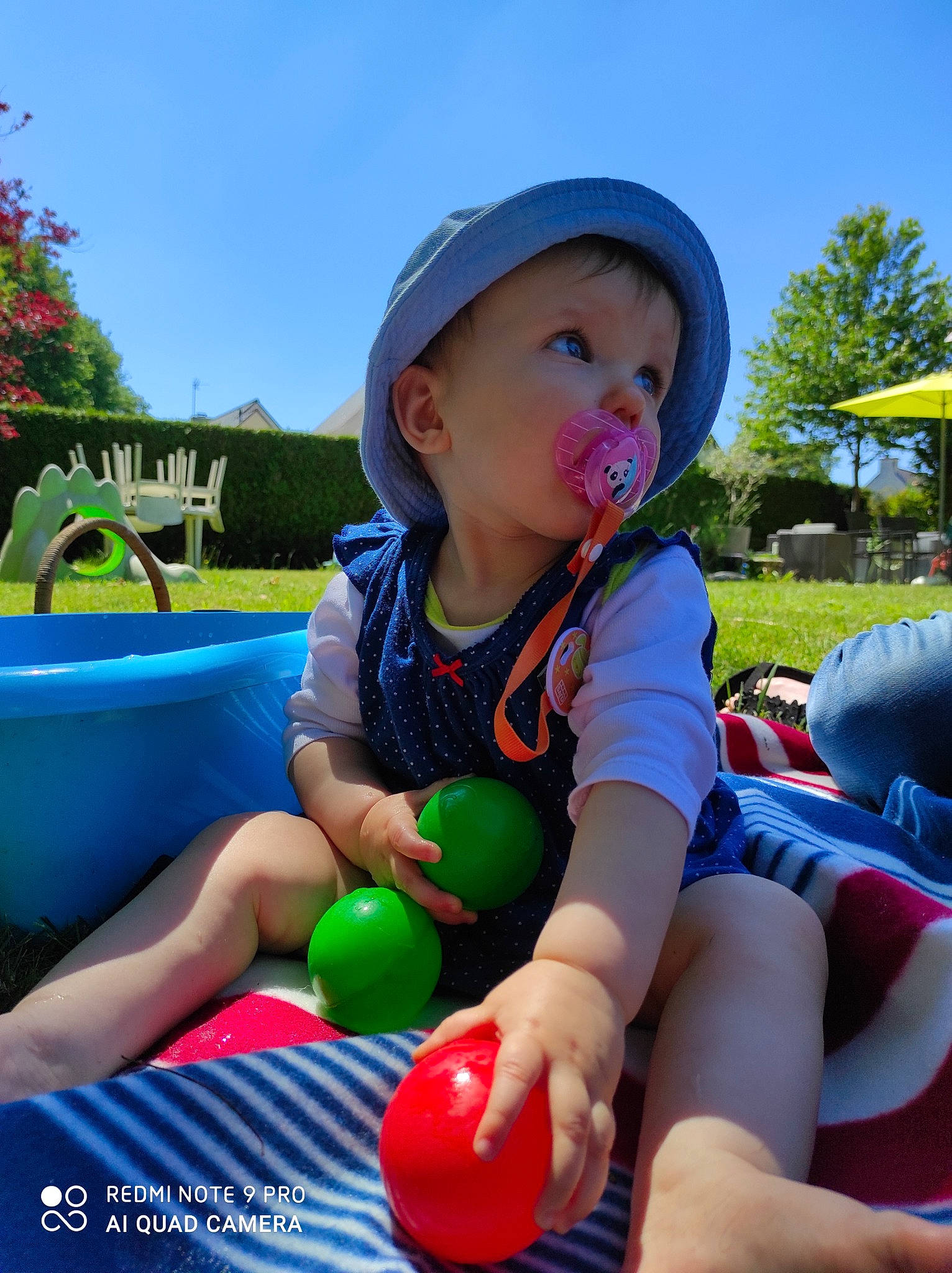 Maelys a rejoint le concours — aidez-le/la à gagner de superbes lots ! baby, baby_toddler_clothing, blue, child, facial_expression, fun, grass, happy, hat, leisure, light, outdoor_recreation, person, plant, playground, recreation, sky, summer, toddler, tree